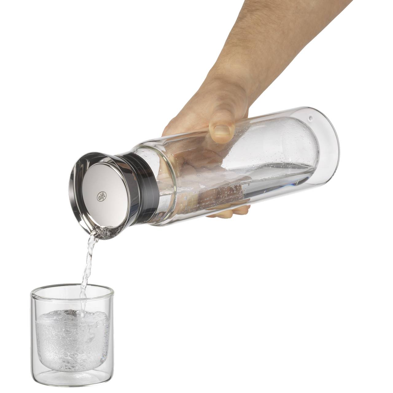 Eine Hand hält einen transparenten Behälter, aus dem eine Flüssigkeit in ein darunter stehendes Glas gegossen wird. Die Flüssigkeit fließt gleichmäßig, und das Glas steht aufrecht auf einer festen Oberfläche.