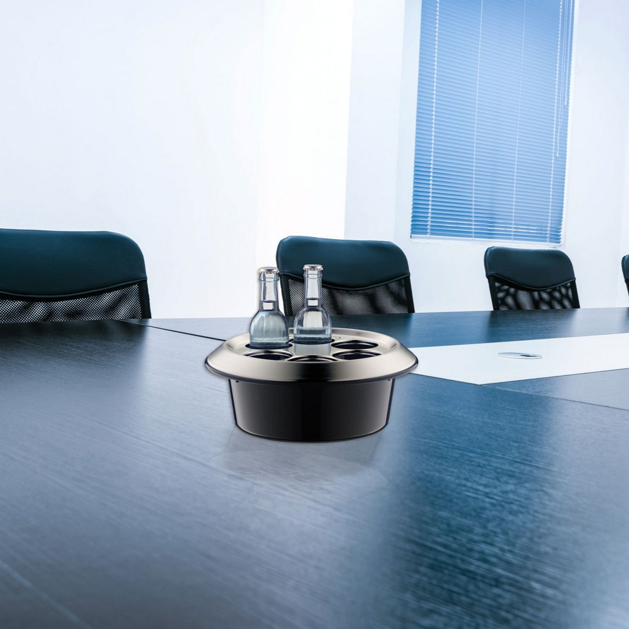 Das Bild zeigt einen modernen Konferenzraum mit einem langen dunklen Tisch und mehreren schwarzen Stühlen. Auf dem Tisch steht ein Tablett mit mehreren Glasflaschen und Gläsern. Der Raum wirkt hell und professionell gestaltet.