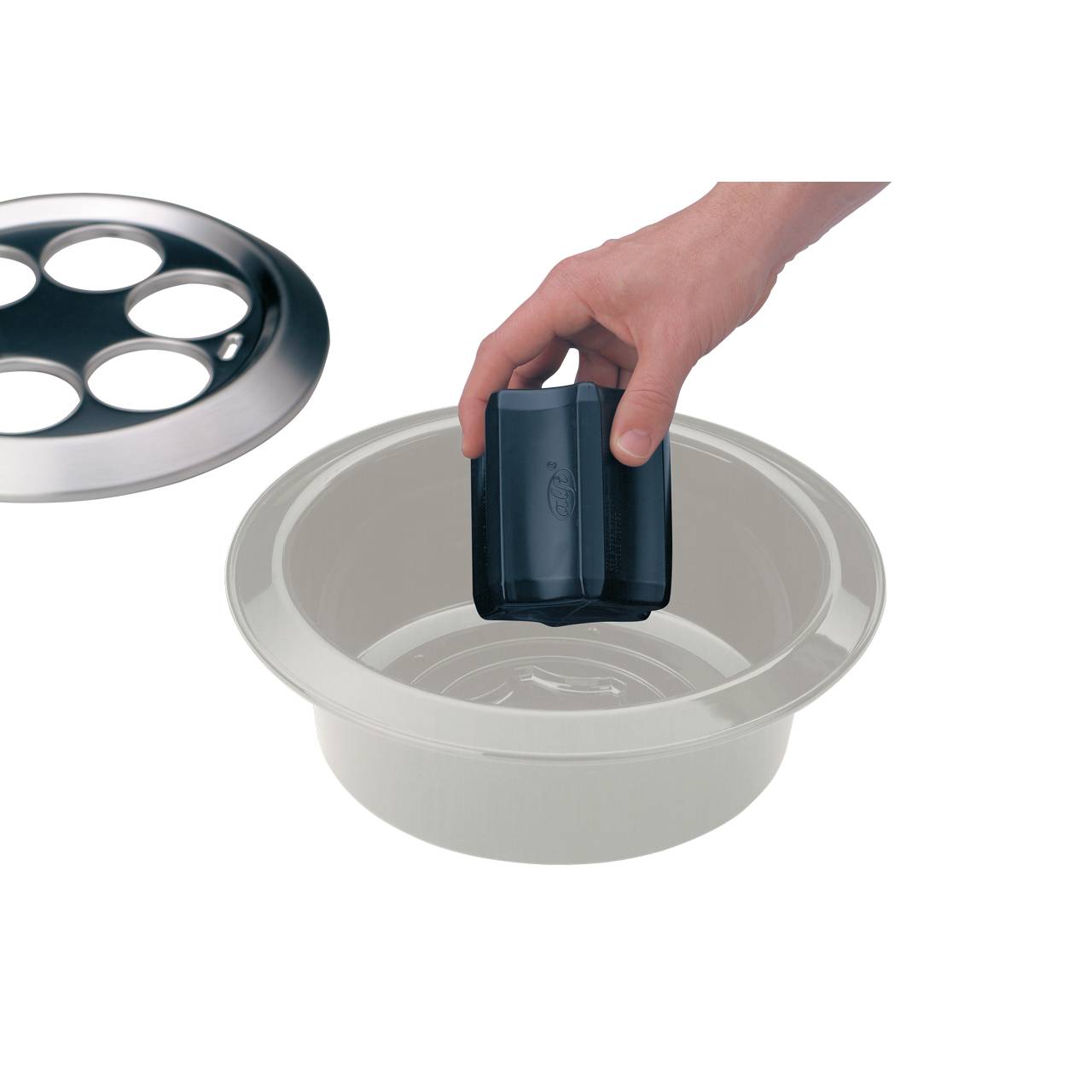 Auf dem Bild befindet sich eine Hand, die ein schwarzes Gefäß in eine weiße Schüssel setzt. Daneben liegt ein Deckel mit mehreren runden Ausschnitten. Die Szene wirkt wie eine Zubereitungssituation in der Küche.