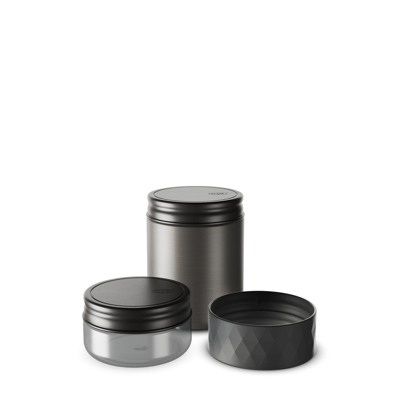 Das Bild zeigt drei zylindrische Dosen in Schwarz und Grau, die auf einer glatten Oberfläche stehen. Zwei der Dosen sind geschlossen und eine hat einen abnehmbaren, geriffelten Deckel. Die Dosen haben ein klares und modernes Design.