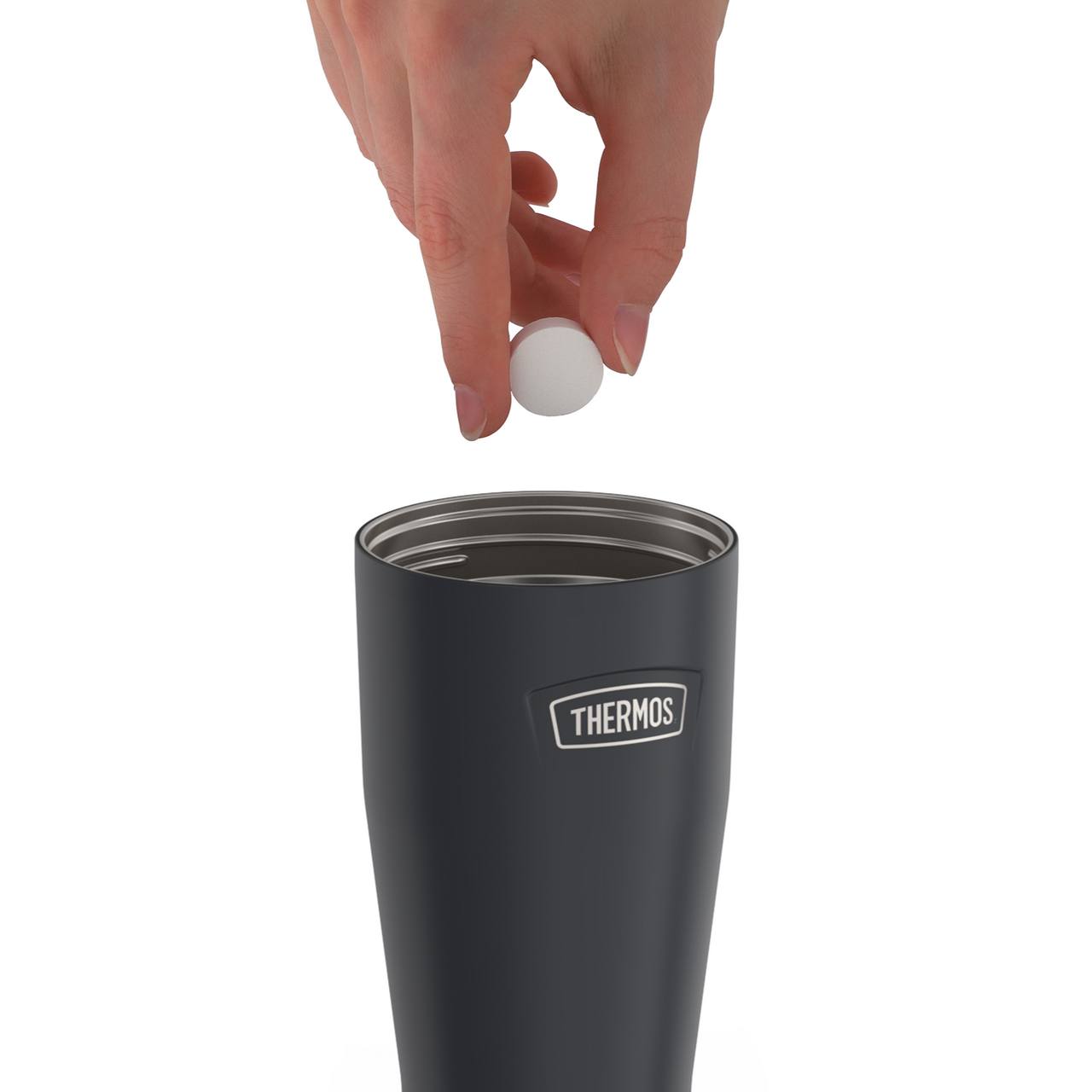 Eine Hand hält eine weiße Tablette über einen schwarzen Becher. Der Becher hat einen Deckel mit der Aufschrift "Camelbak". Der Hintergrund ist weiß.