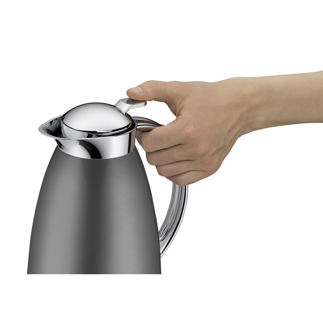 Ein Edelstahl-Wasserkocher mit glatter Oberfläche wird von einer Hand am Griff gehalten. Der Wasserkocher hat eine geschwungene Form und einen glänzenden Deckel. Die Hand greift fest zu.