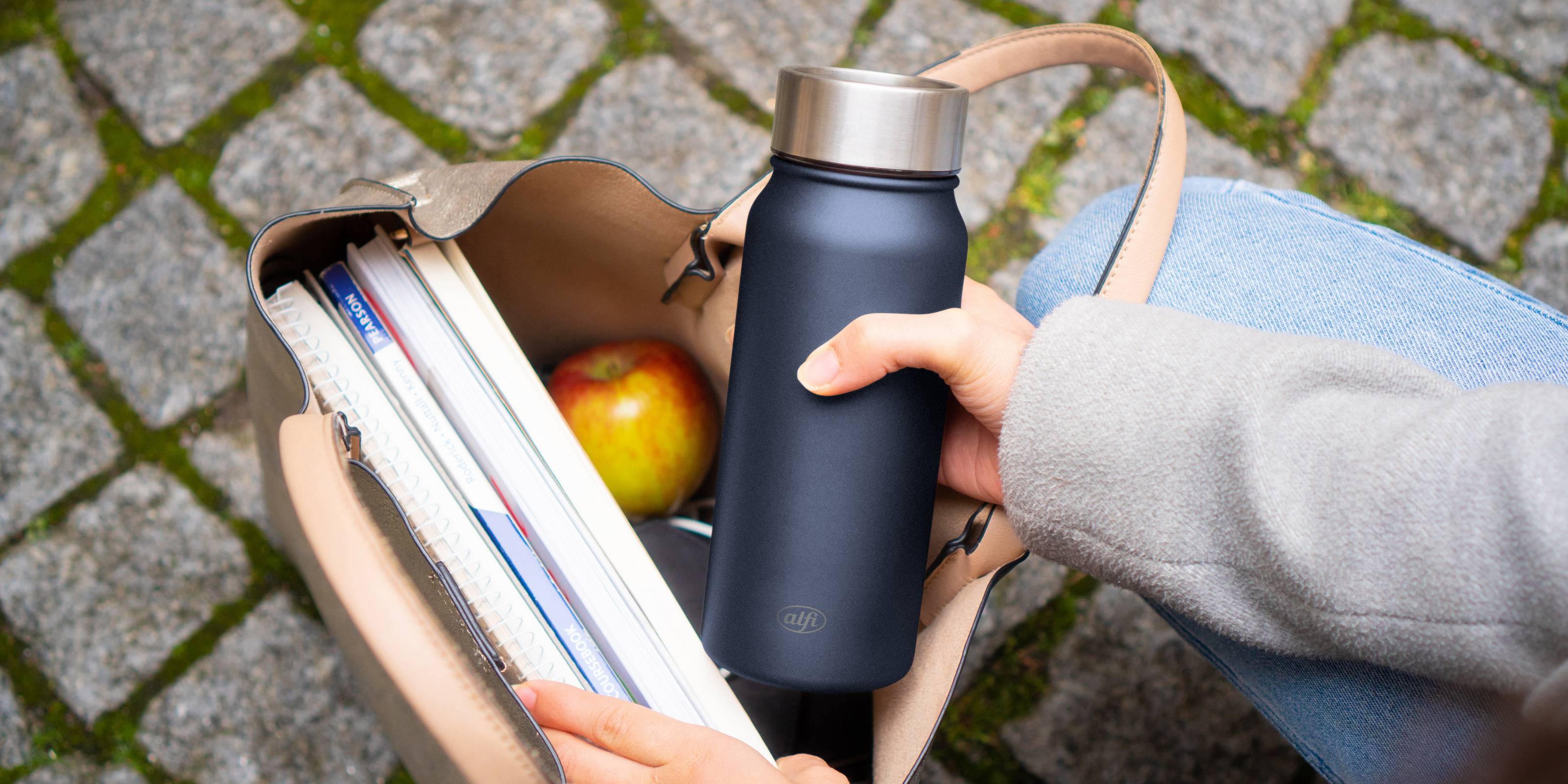 pure drinking mug in hand with books and apple in bag